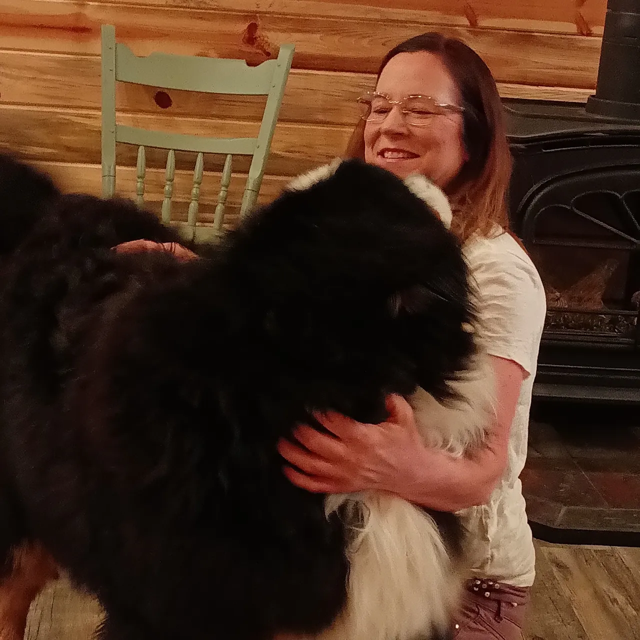 A woman is hugging a dog in front of the fireplace.