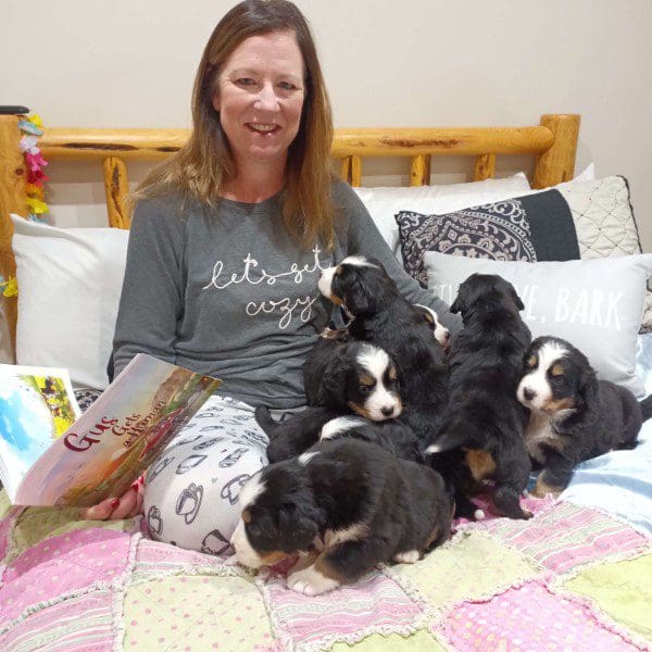 A woman sitting on the bed with her six puppies.