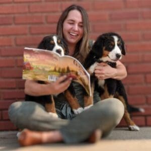 A woman sitting on the ground with two dogs.