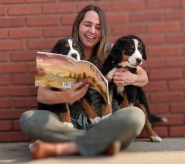 A woman sitting on the ground with two dogs.